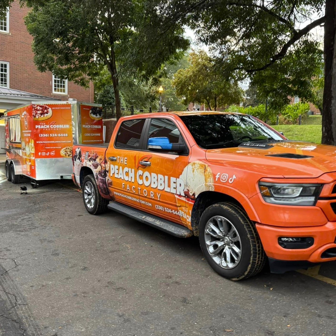 Orange truck towing a Peach Cobbler trailer parked on a tree-lined street
