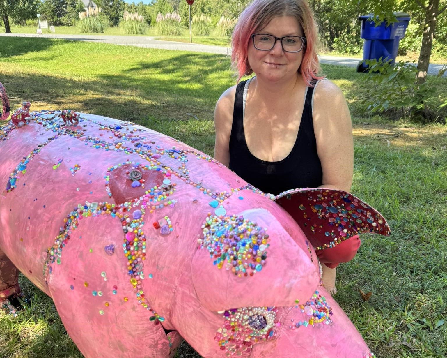 Woman sitting beside a pink, glitter-covered sculpture in a grassy park