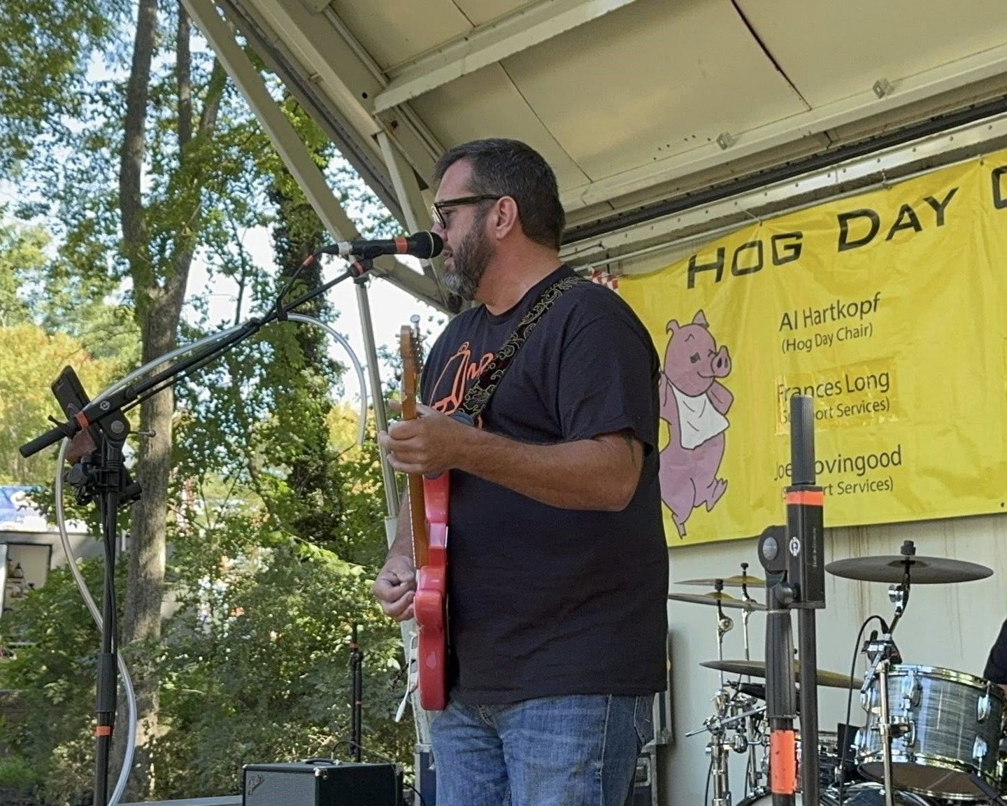 Man playing red guitar and singing on an outdoor stage at a Hot Day event