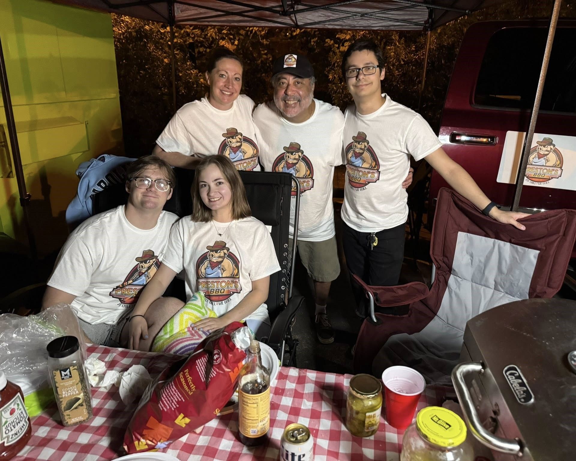 Four people posing at a table with drinks in a festive outdoor tent setting