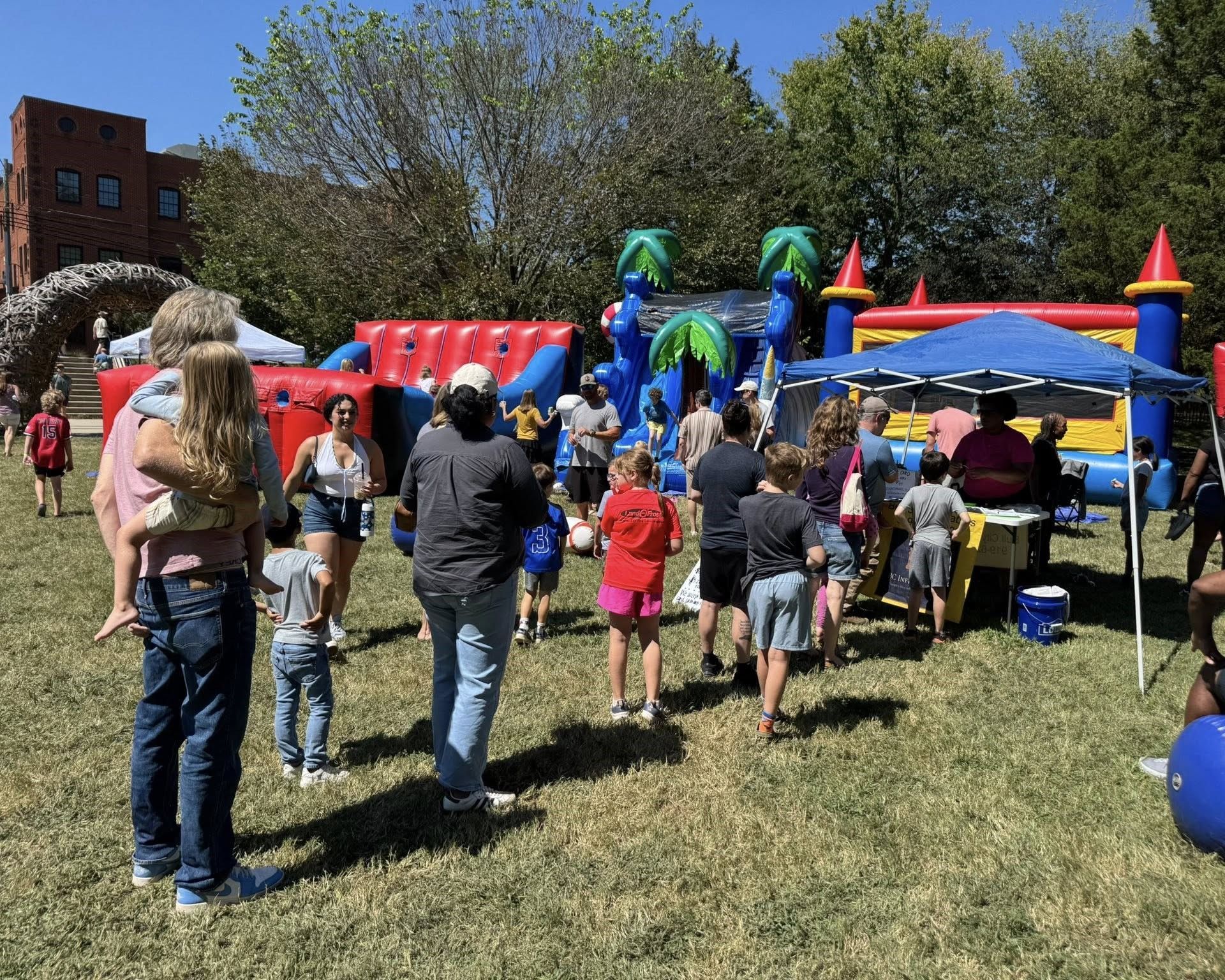 People gathered at a colorful outdoor bounce house event on a grassy field.