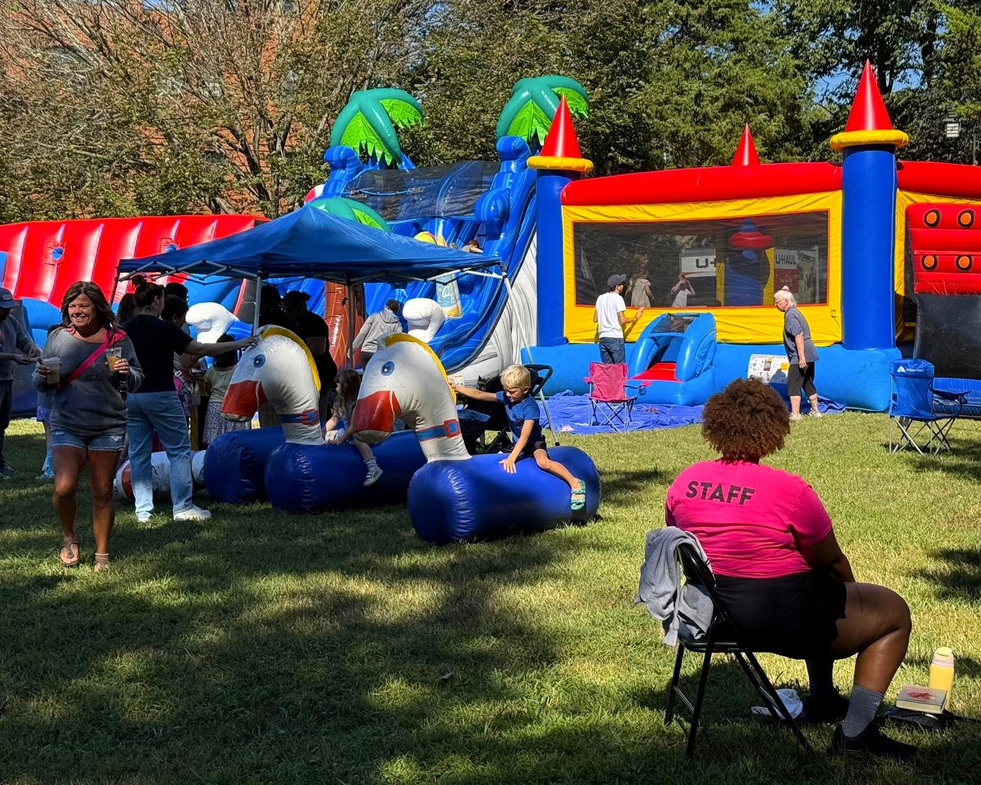 Children playing on a blue inflatable bounce house and slide at an outdoor park event.