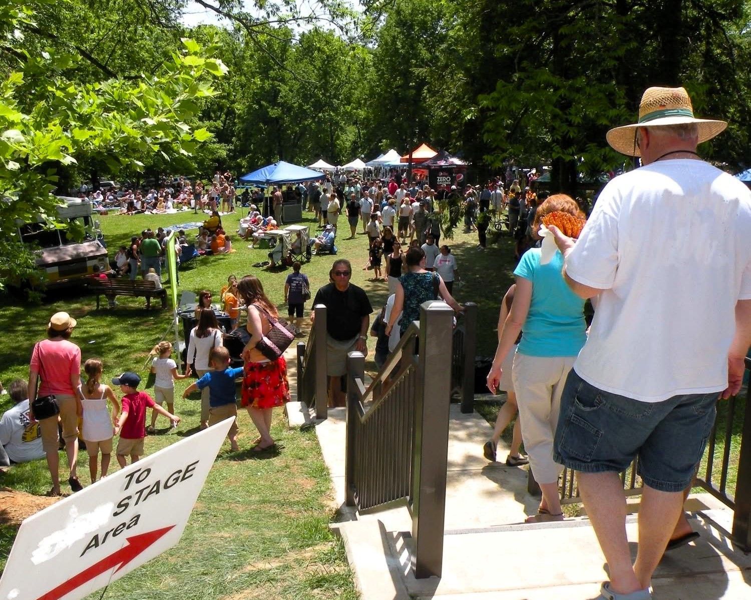 People walking down steps into a crowded outdoor park event on a sunny day.