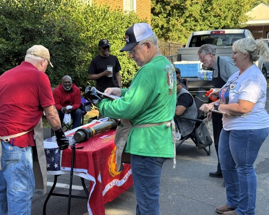 People gathered around a red table outdoors, passing out items at a community event.