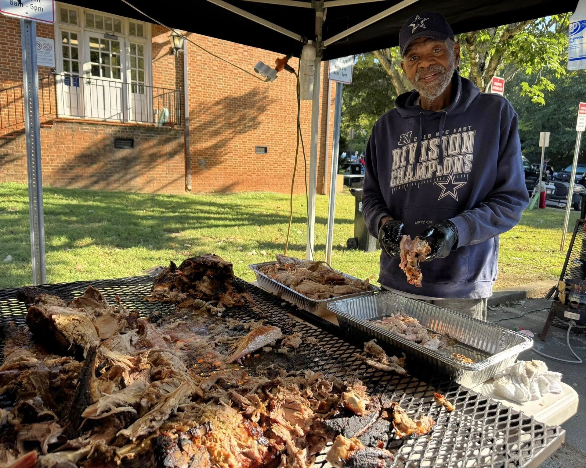 Man grilling meat outdoors at a backyard cookout beside a brick house.