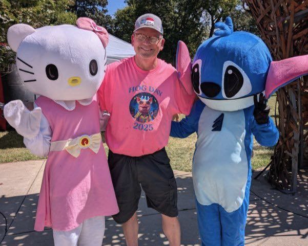 Person posing between Hello Kitty and Stitch mascots outdoors, wearing a pink shirt and cap.