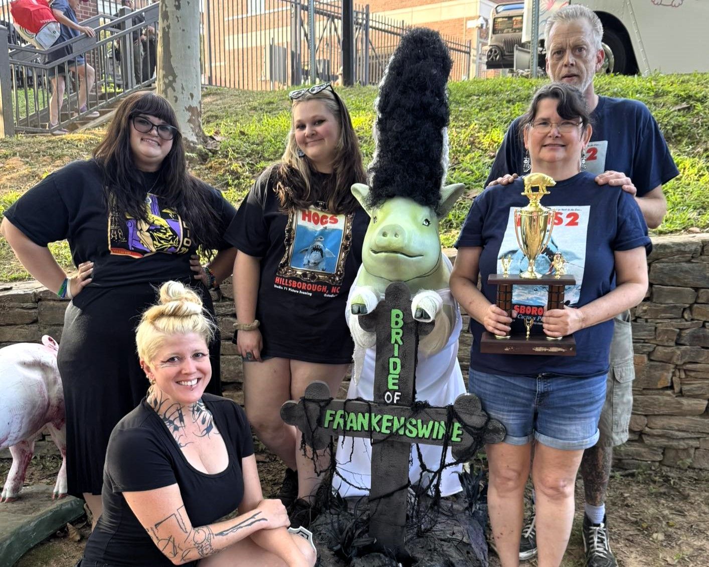 Group posing with a green Frankenstein figure in front of a haunted-style display, holding trophies and awards.