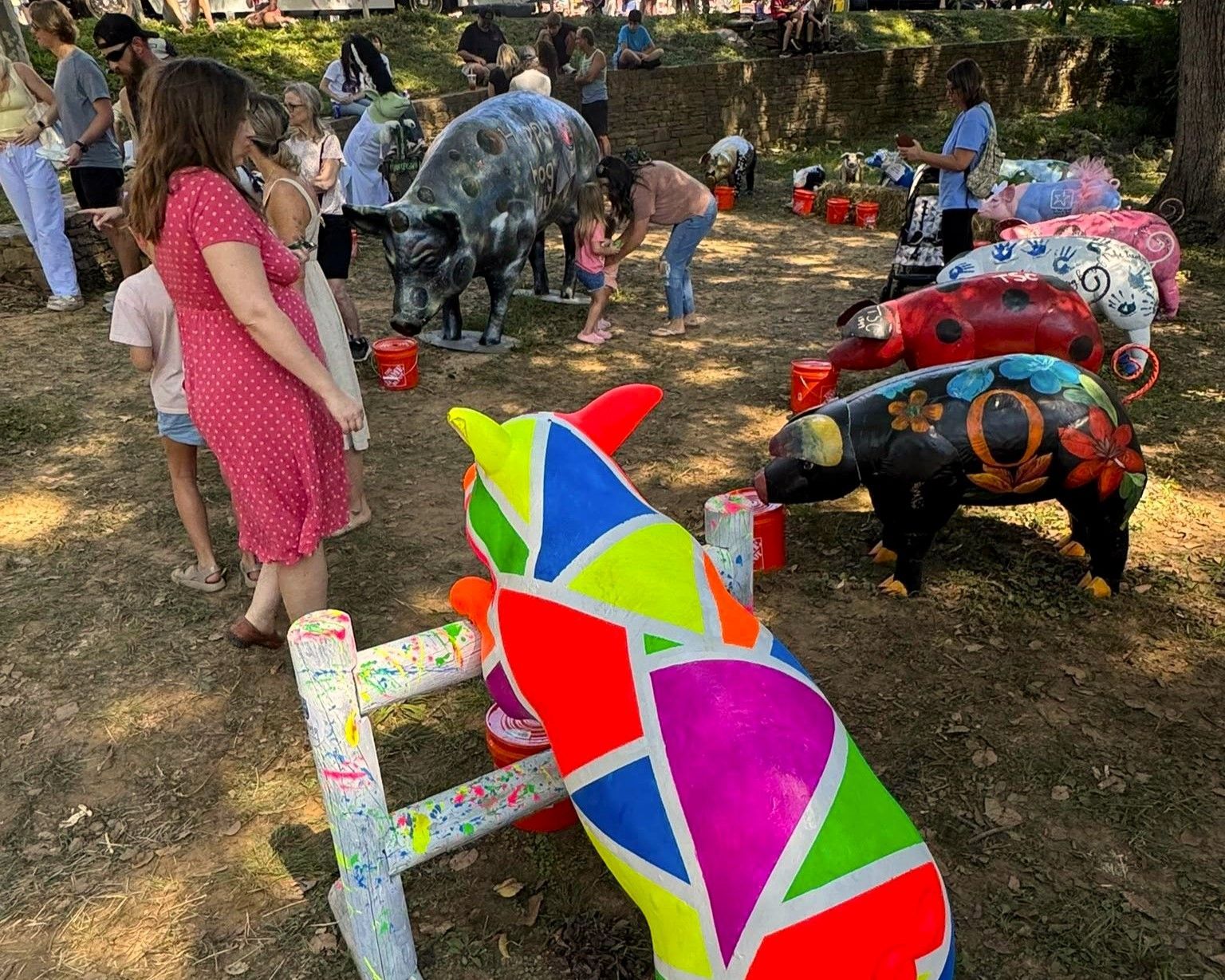 Colorful painted cow sculptures outdoors, with people walking among them on a sunny day.