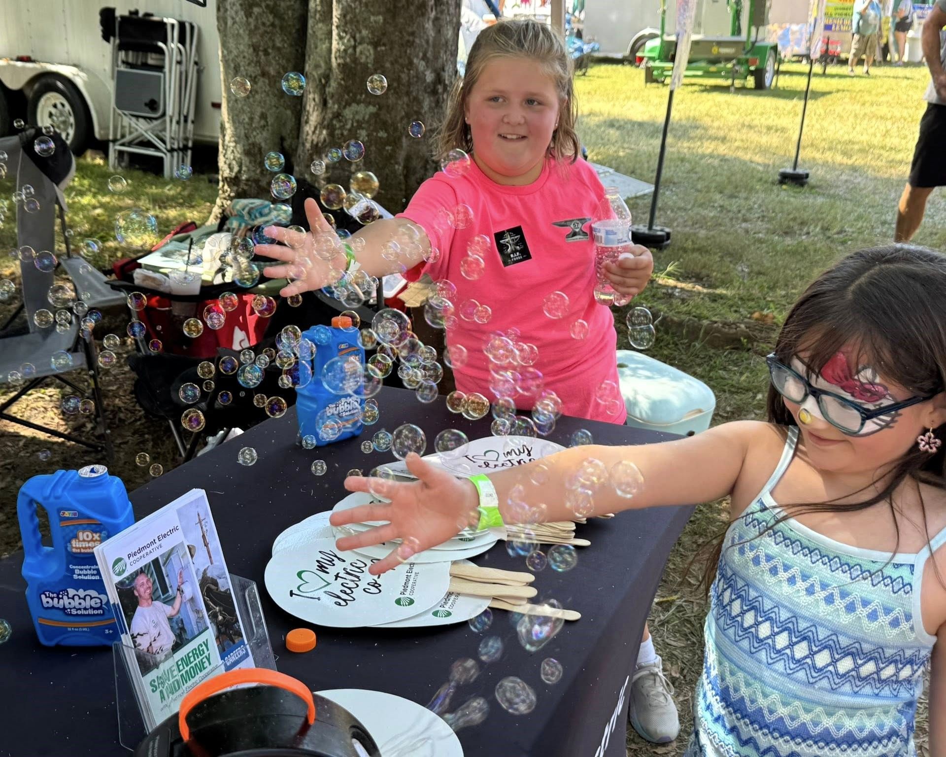Children with painted hands at an outdoor table, smiling and showing their crafts