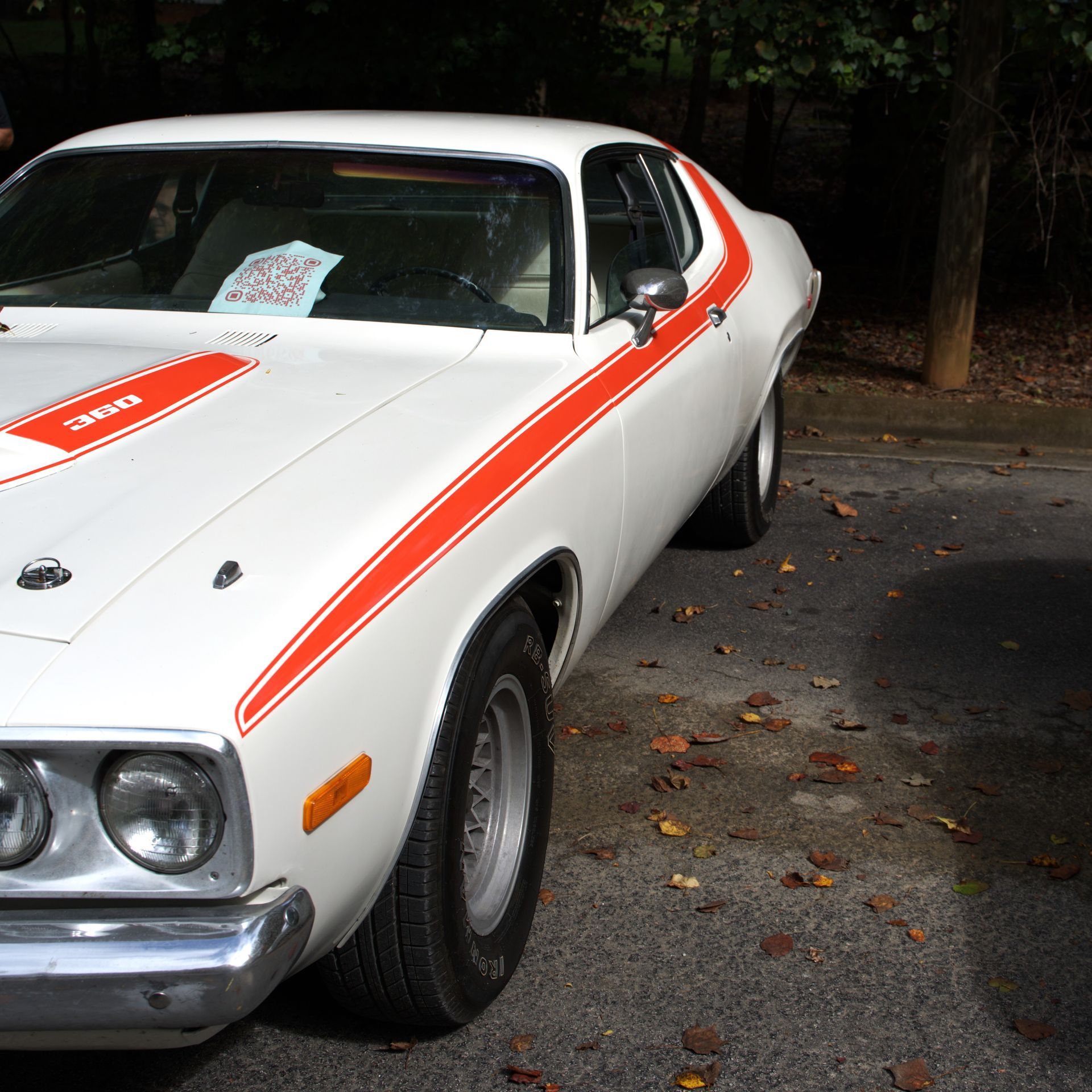 White classic muscle car with orange racing stripes parked outdoors near trees