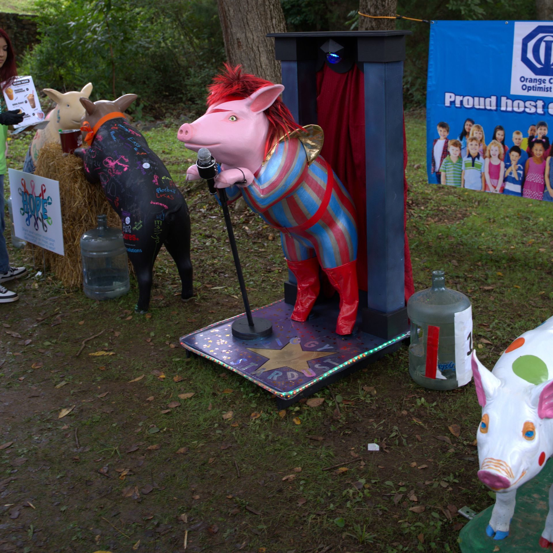Colorful animal statues on stands in a grassy outdoor display, including a pink pig and white cow.