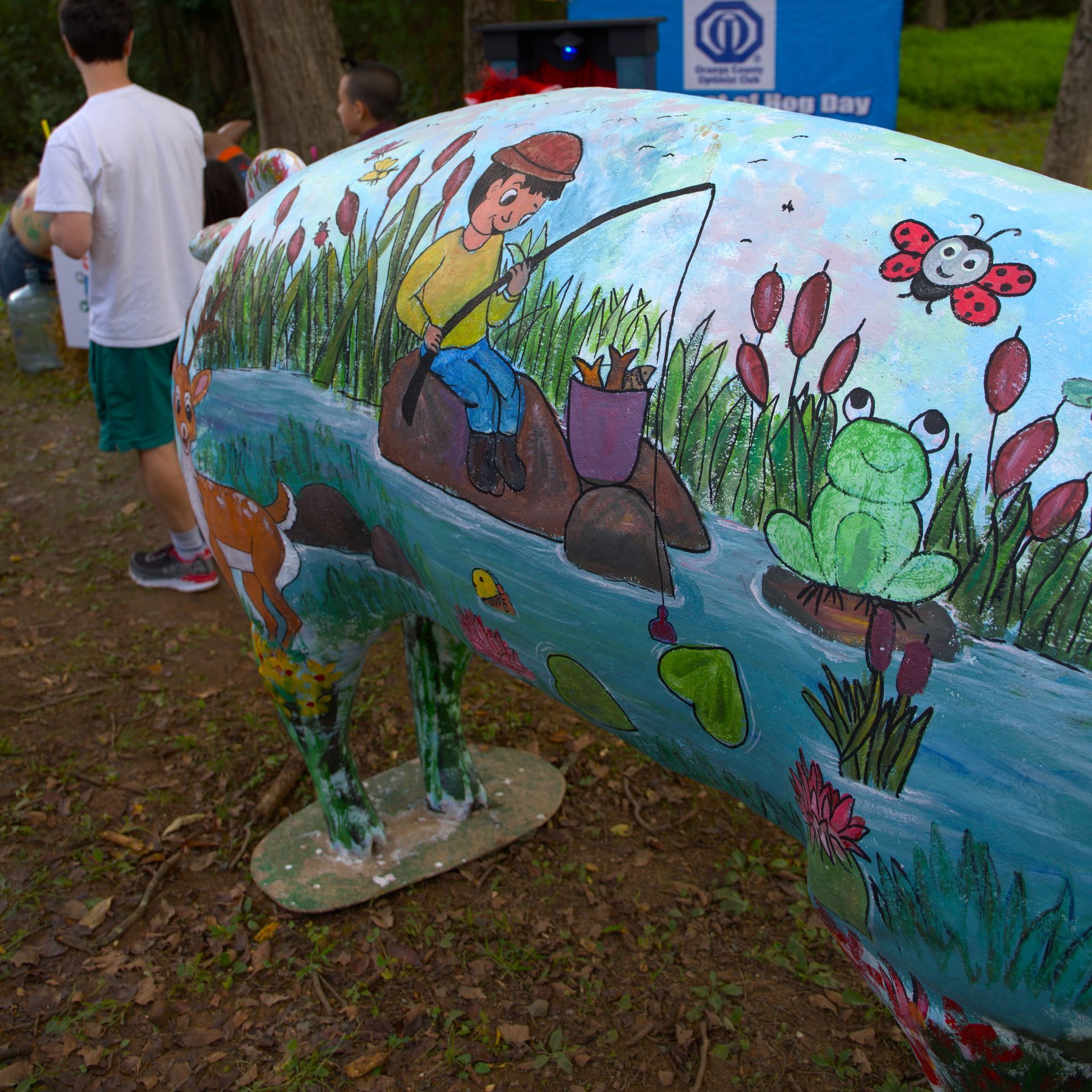Colorful painted sculpture of a snail in a park, decorated with a gardener, flowers, and a frog.