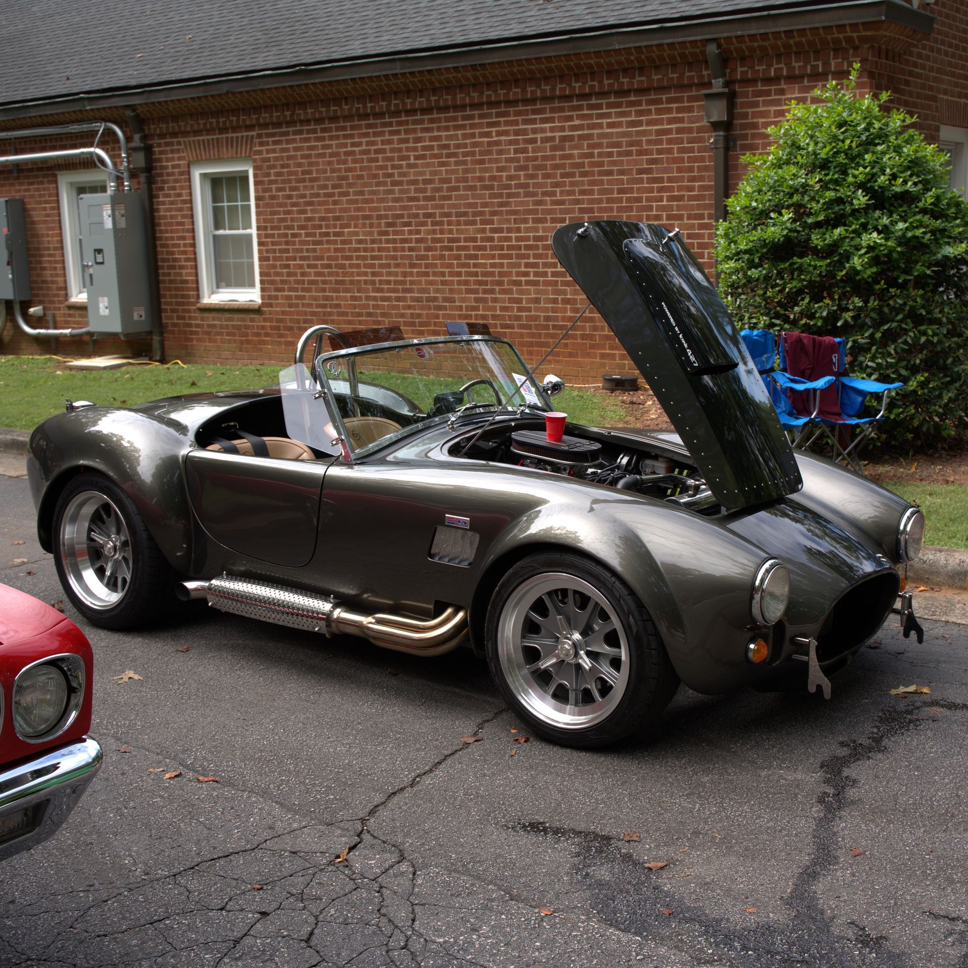 Gray vintage convertible sports car with hood raised, parked beside a brick building