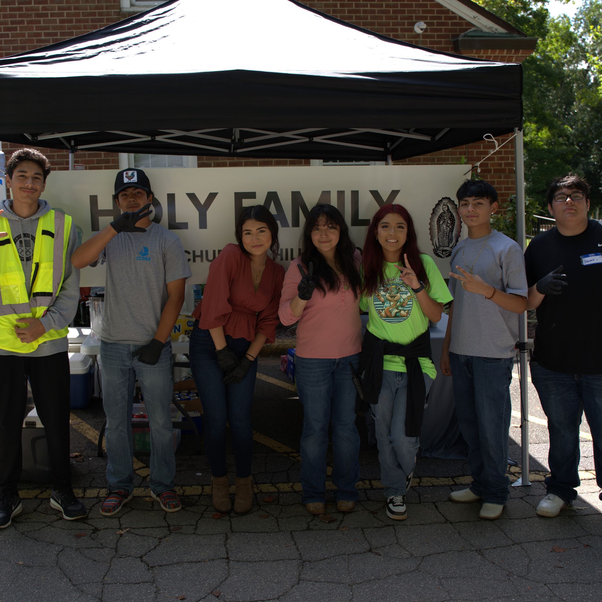 Group of people standing under a black canopy at an outdoor event, posing in front of a banner.