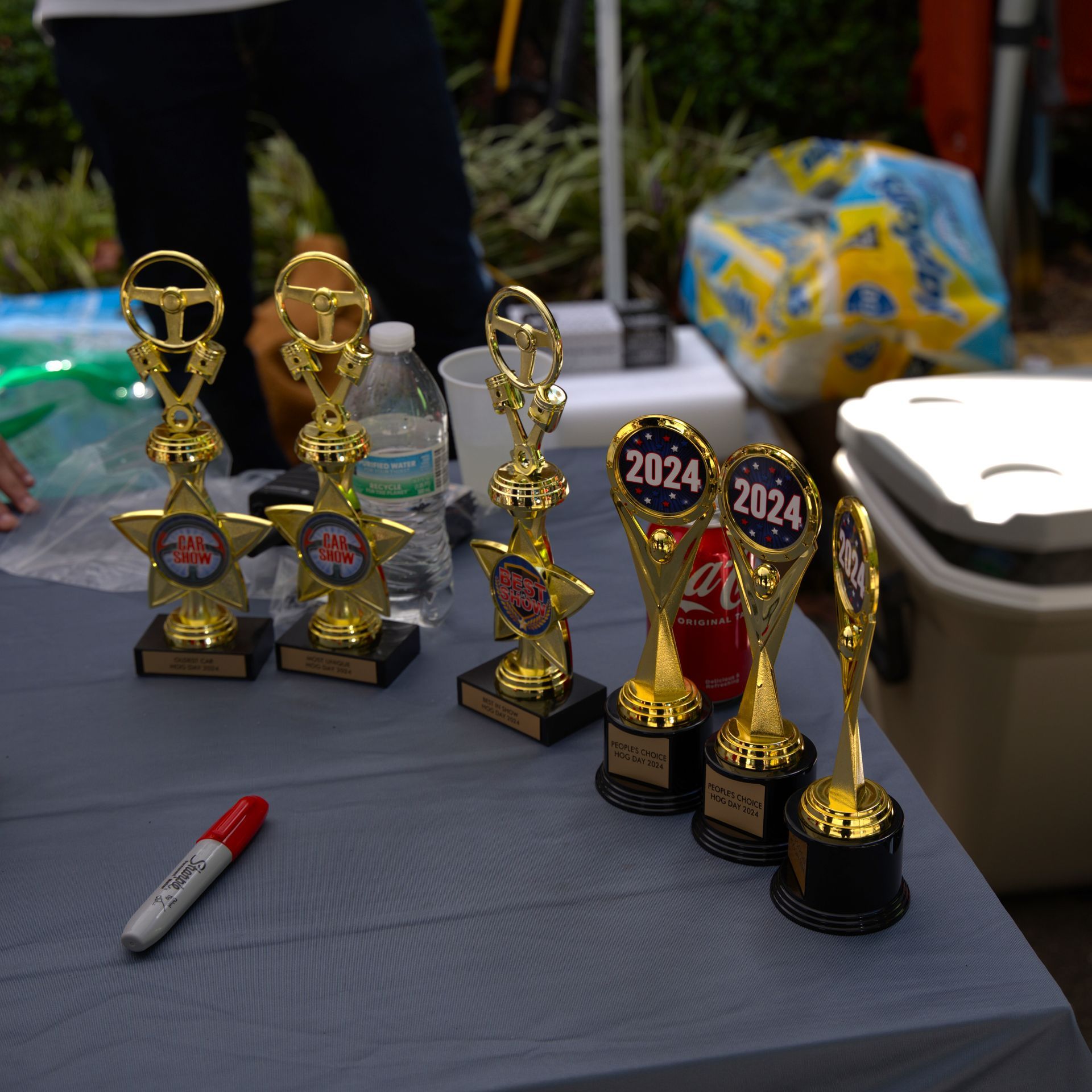 Trophy display on a table with several gold and red awards, a marker, and a water bottle nearby