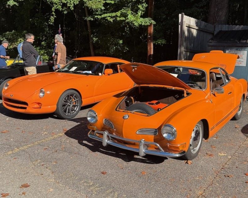 Two orange classic sports cars parked outdoors, one with its hood open.