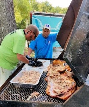 Cooks chopping BBQ pork on a smoker grill
