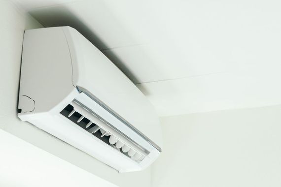 White air conditioning unit mounted on a wall with black tubing extending to an outdoor unit. Door visible.