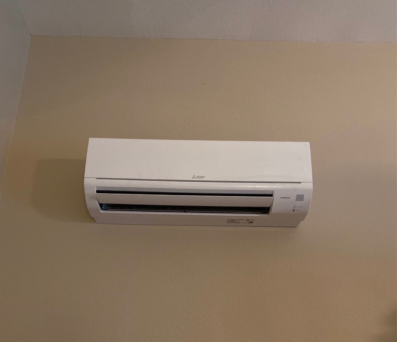 White wall-mounted air conditioner on a pale blue wall in a room, next to a window with a white curtain.