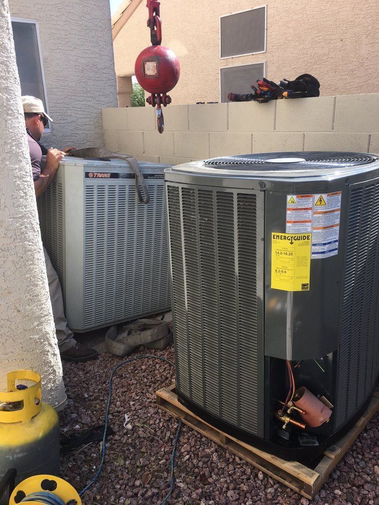 HVAC units being lifted by a crane on a pallet; a worker oversees the installation.