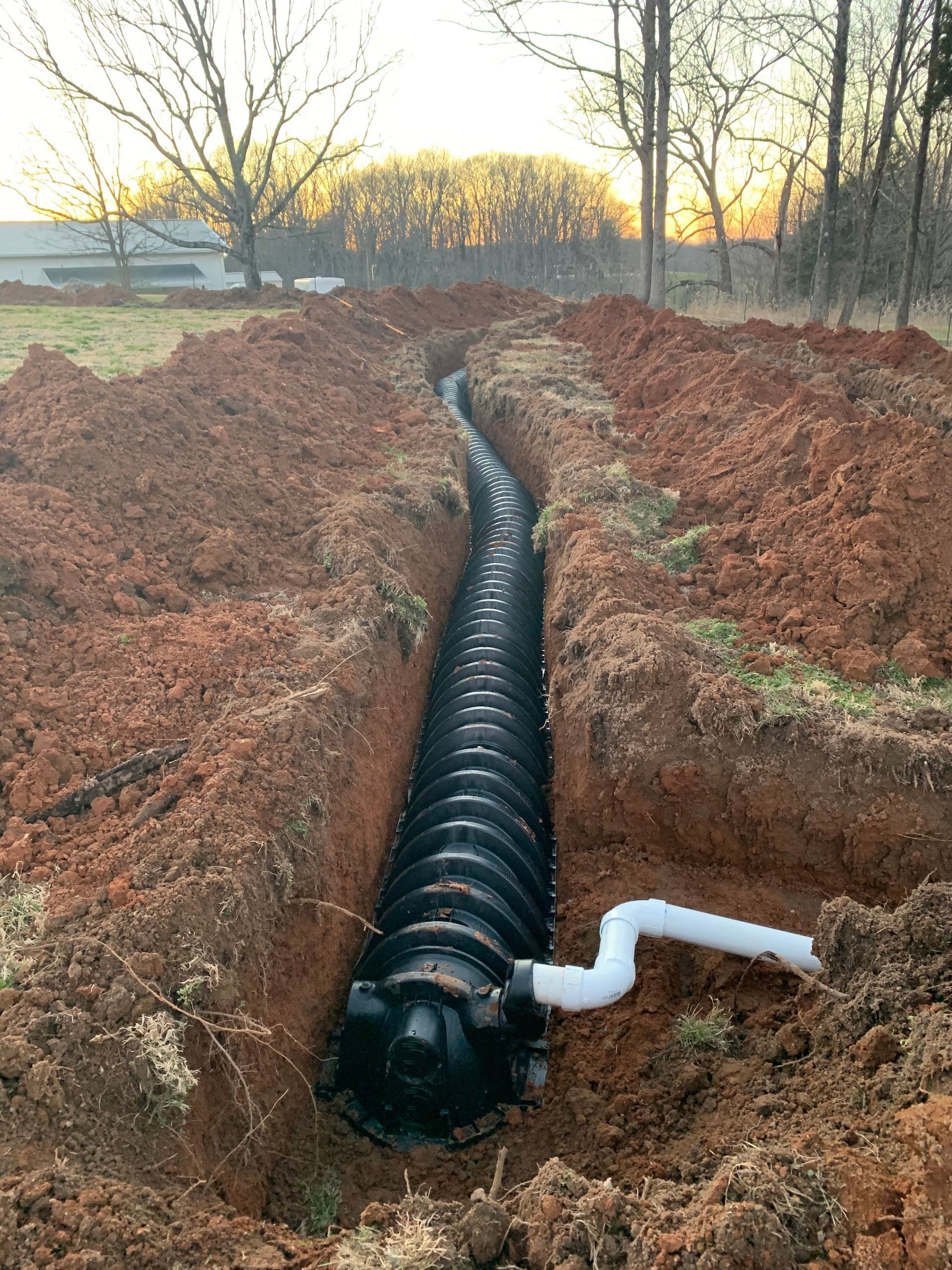 A black corrugated plastic septic chamber installed in a dirt trench with a white pipe leading into it.