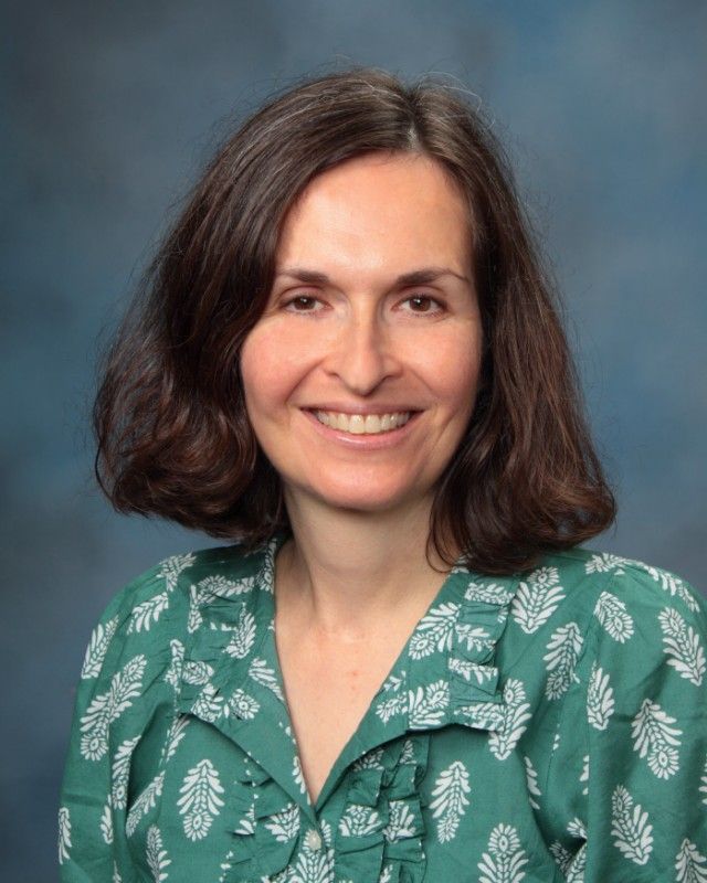 Woman smiling, wearing a green patterned blouse, against a blue background.