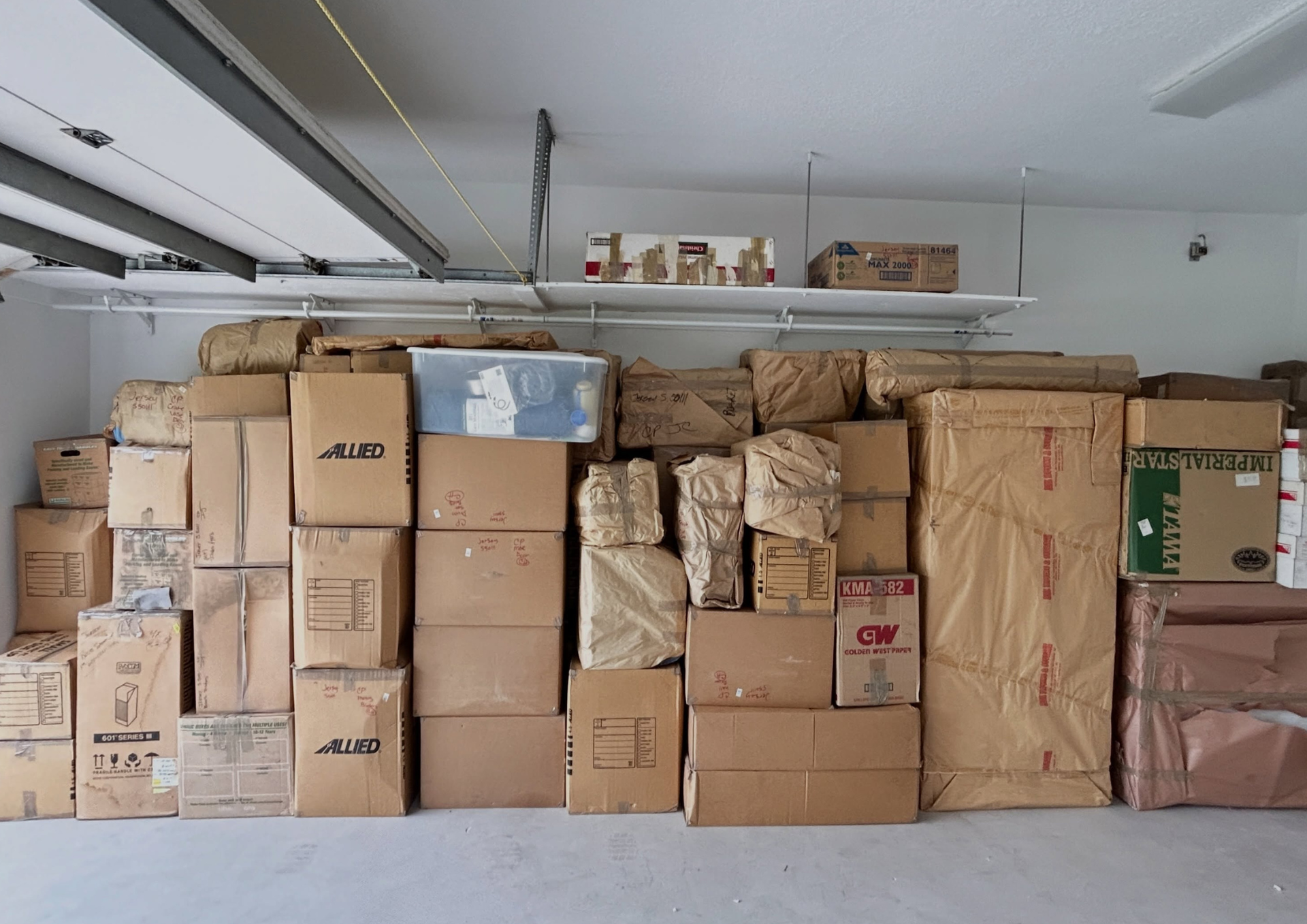 Stacked cardboard boxes in a bright empty room with large windows and carpeted floor