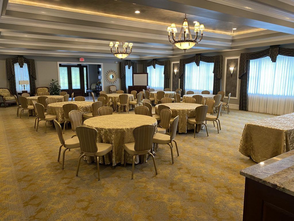 A banquet hall with round, gold-covered tables and chairs arranged for an event, lit by two decorative chandeliers.