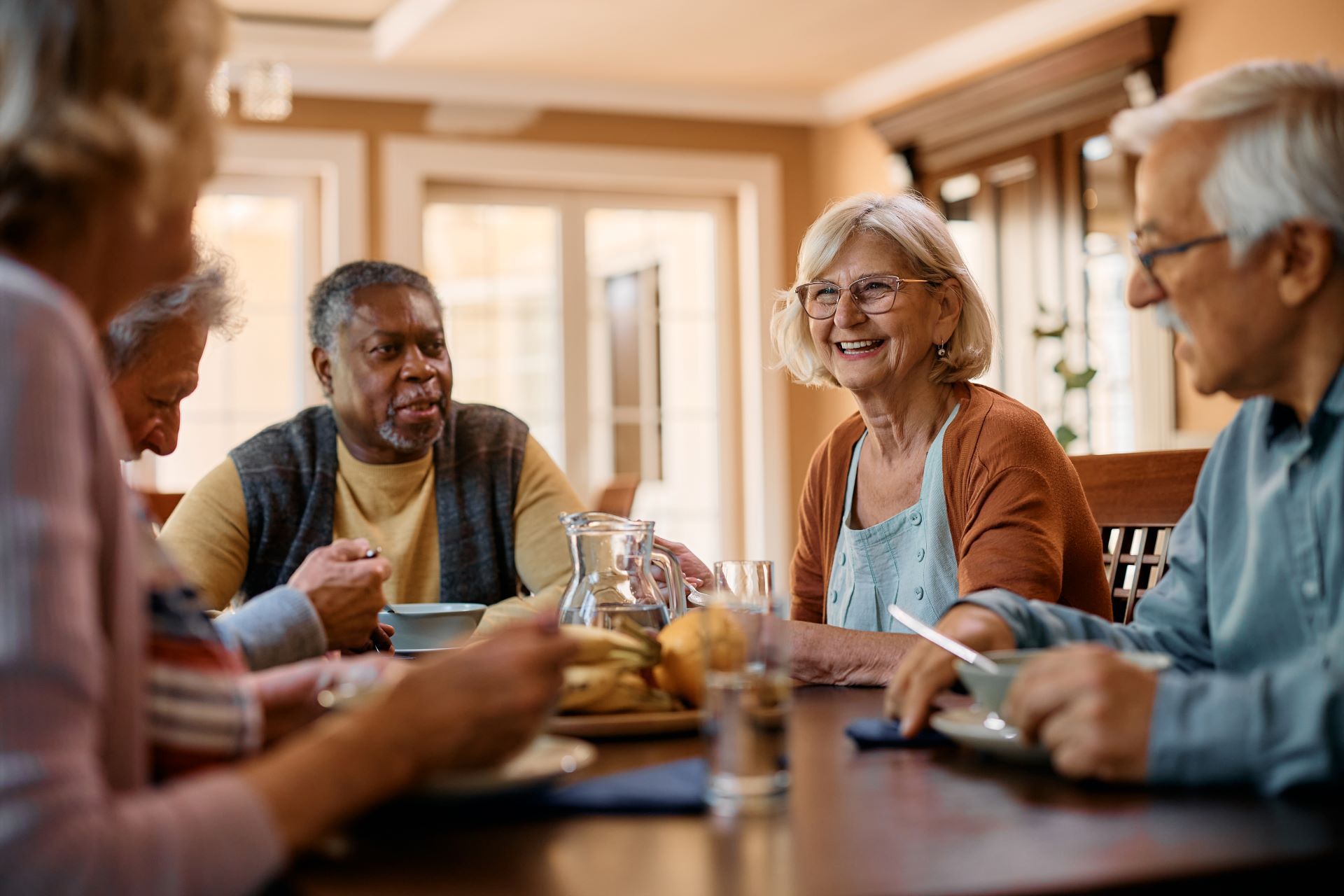 A group of people sitting around a table having a conversation in a brightly lit dining room.