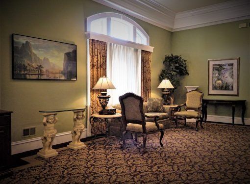 A quiet, traditionally styled room with olive walls, patterned carpet, antique chairs, two lamps, and landscape paintings.