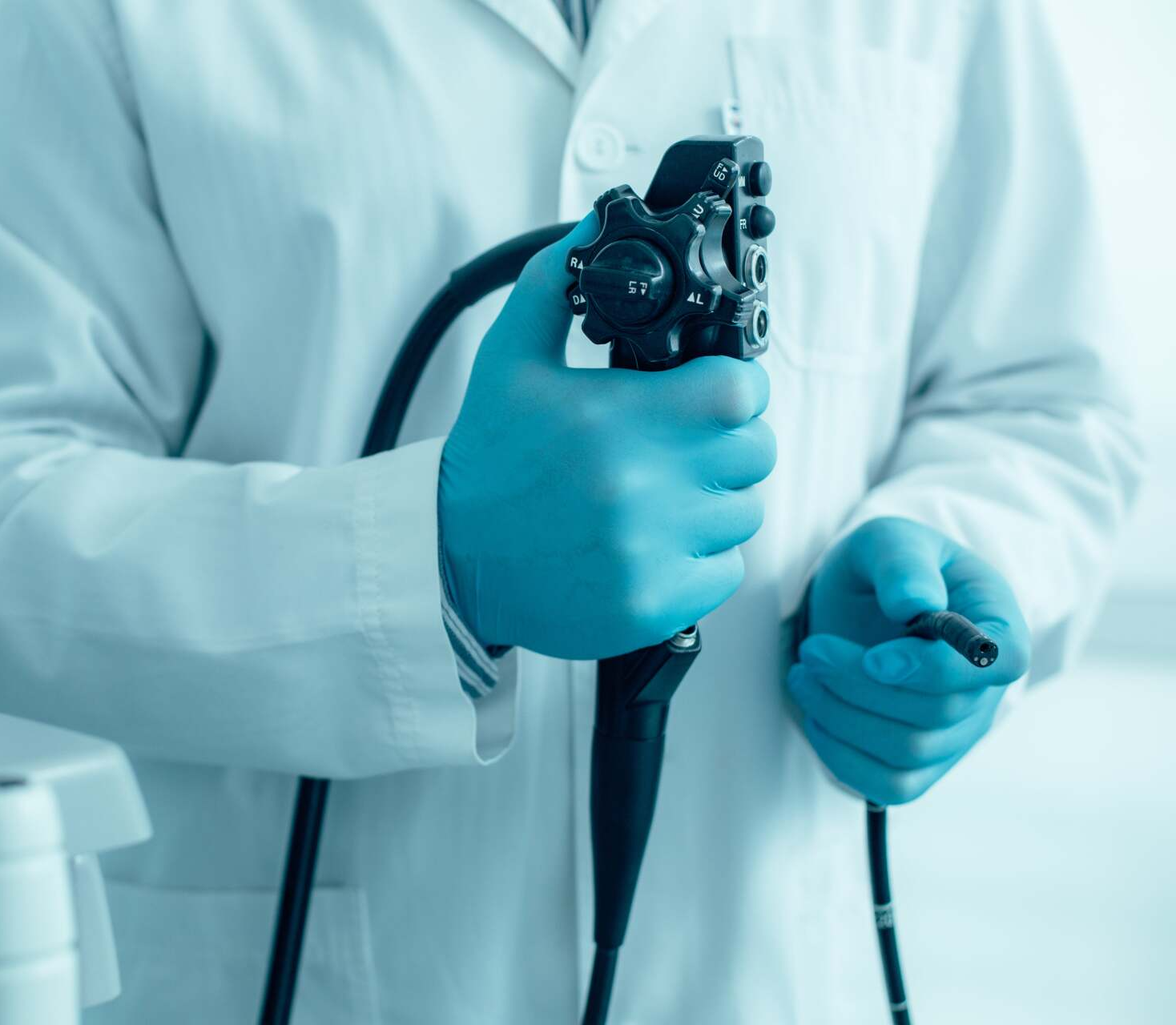 A doctor wearing blue gloves is holding an endoscope in his hands.