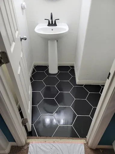Small bathroom with black hexagonal floor tiles, white pedestal sink, black faucet, and white walls.