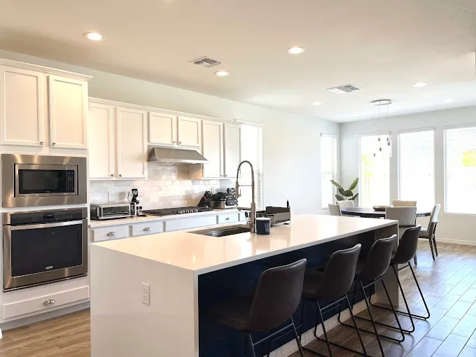 Modern kitchen with white cabinets, blue island, stainless steel appliances, and wooden floor.