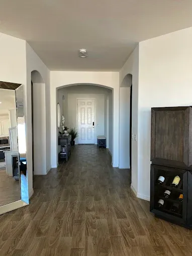 Hallway with wood-look tile floor, white walls, and arched doorways leading to a front door and a wine cabinet.