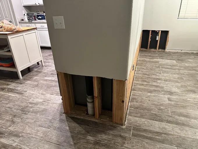 Kitchen island with exposed framing and drywall. Plumbing visible. Damaged wall section in the background.