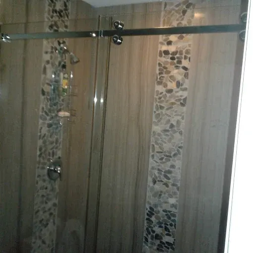 Shower with glass sliding doors, stone accents, and brown tile.
