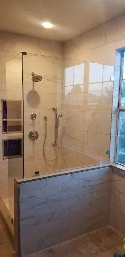 A newly renovated shower with glass doors, tiled walls, and a built-in shelf.