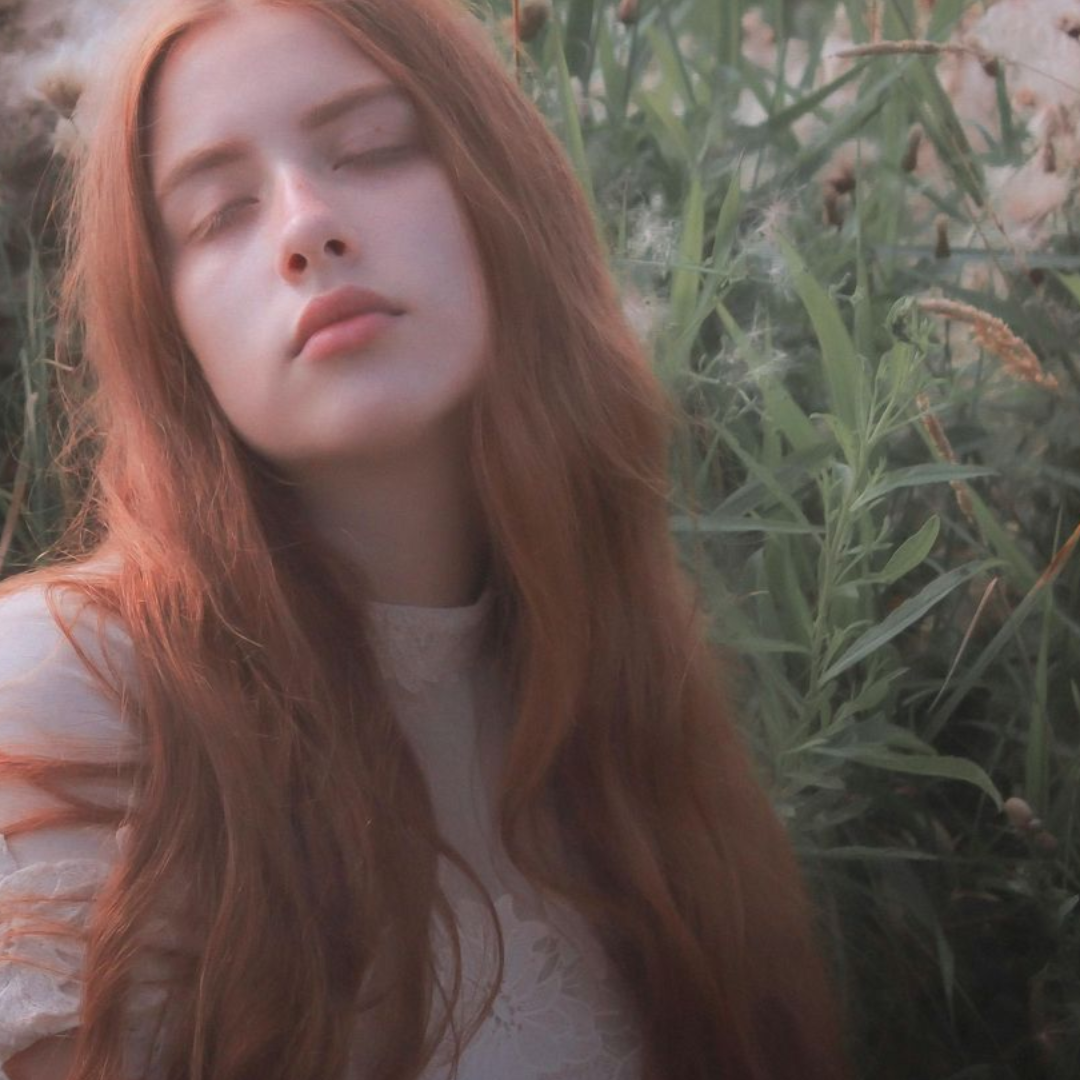 woman with long, red hair dreamily basking in a sunny field of milkweed