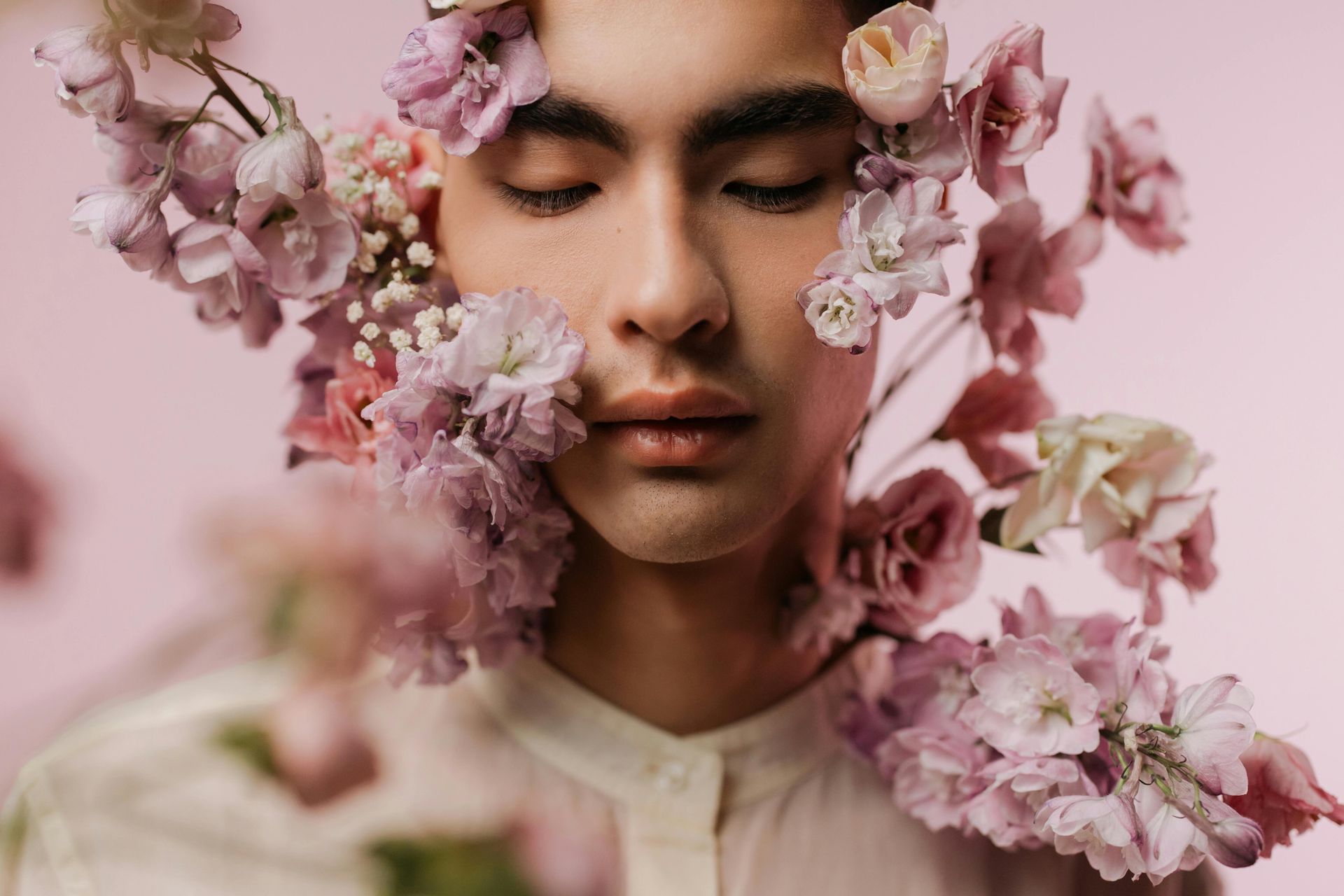 man's face close up with pink flowers around him.