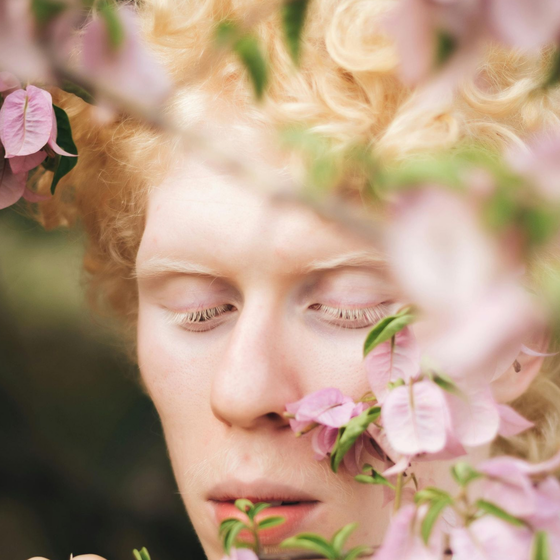 non-binary human with portrait up close standing behind a cherry blossom tree