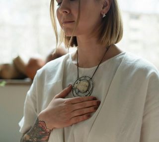 Woman with hand on chest, wearing necklace, eyes closed.