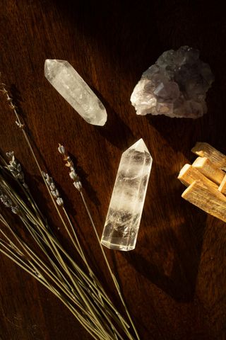 Crystals, dried lavender, and palo santo sticks on a dark wooden surface, bathed in sunlight.