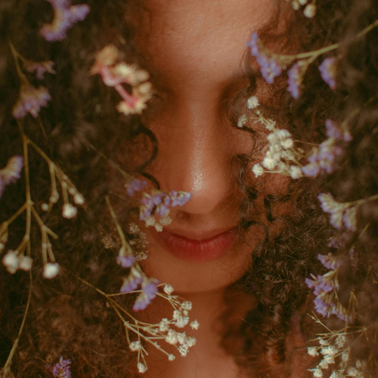 up close image of a woman with curly hair and flowers in it, eyes closed