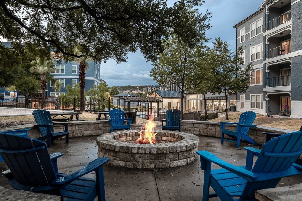 a fire pit surrounded by blue chairs in front of a building at Marquis at Crown Ridge in San Antonio, TX.