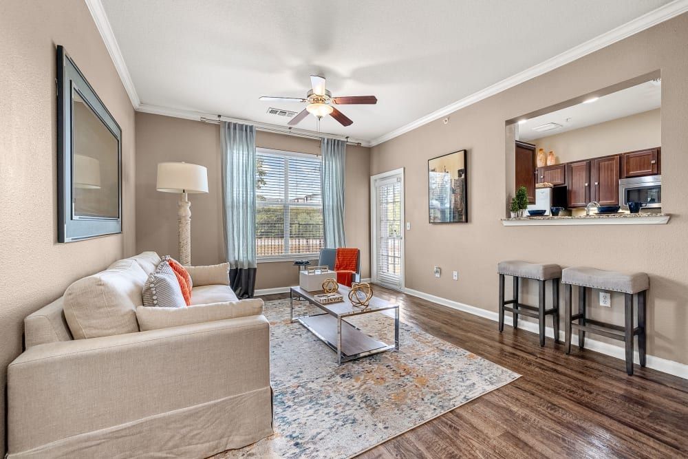 a living room with a couch, coffee table, stools, and a ceiling fan at Marquis at Crown Ridge in San Antonio, TX.