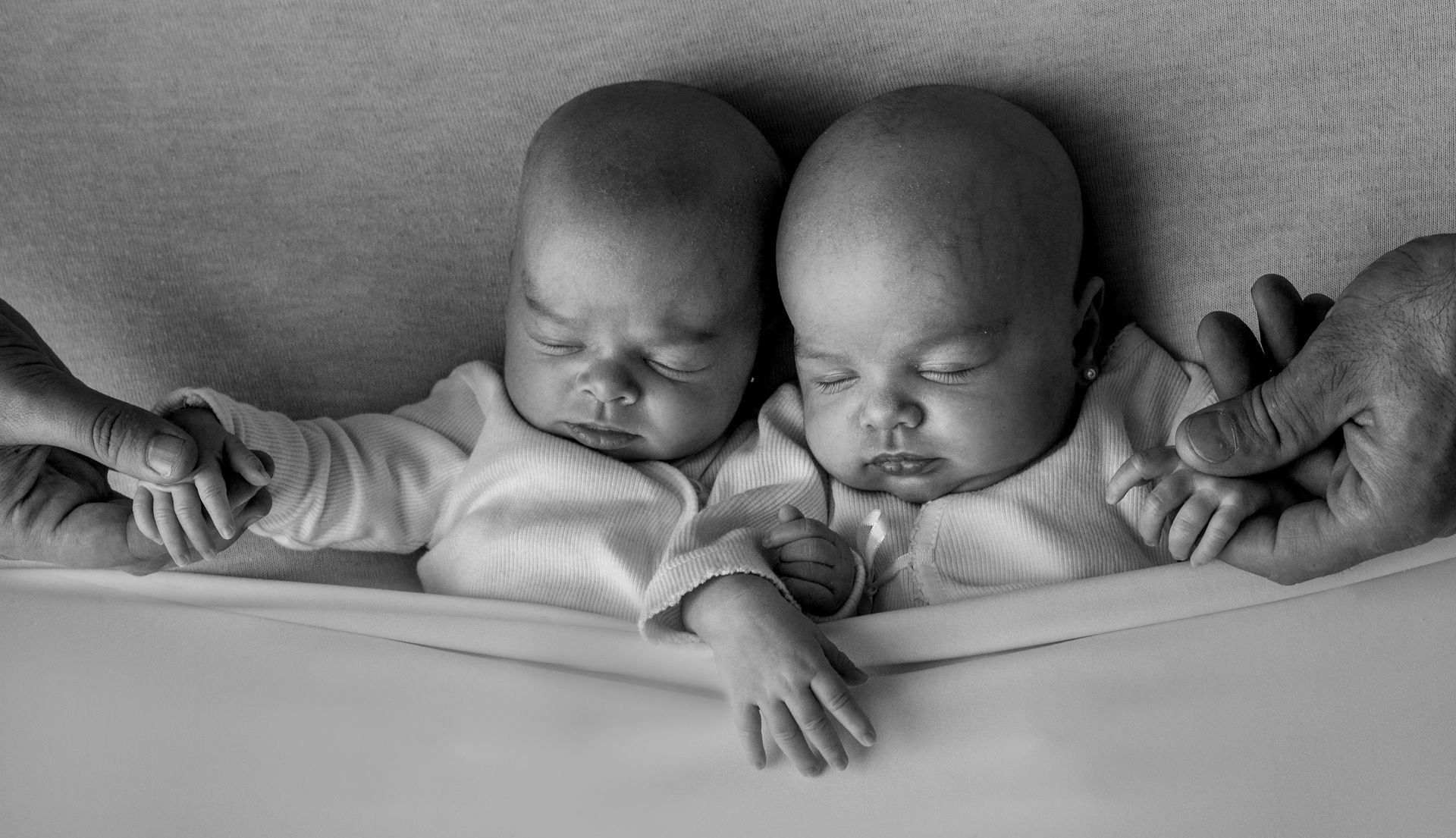 Due neonati addormentati giacciono fianco a fianco in una culla, avvolti in coperte.