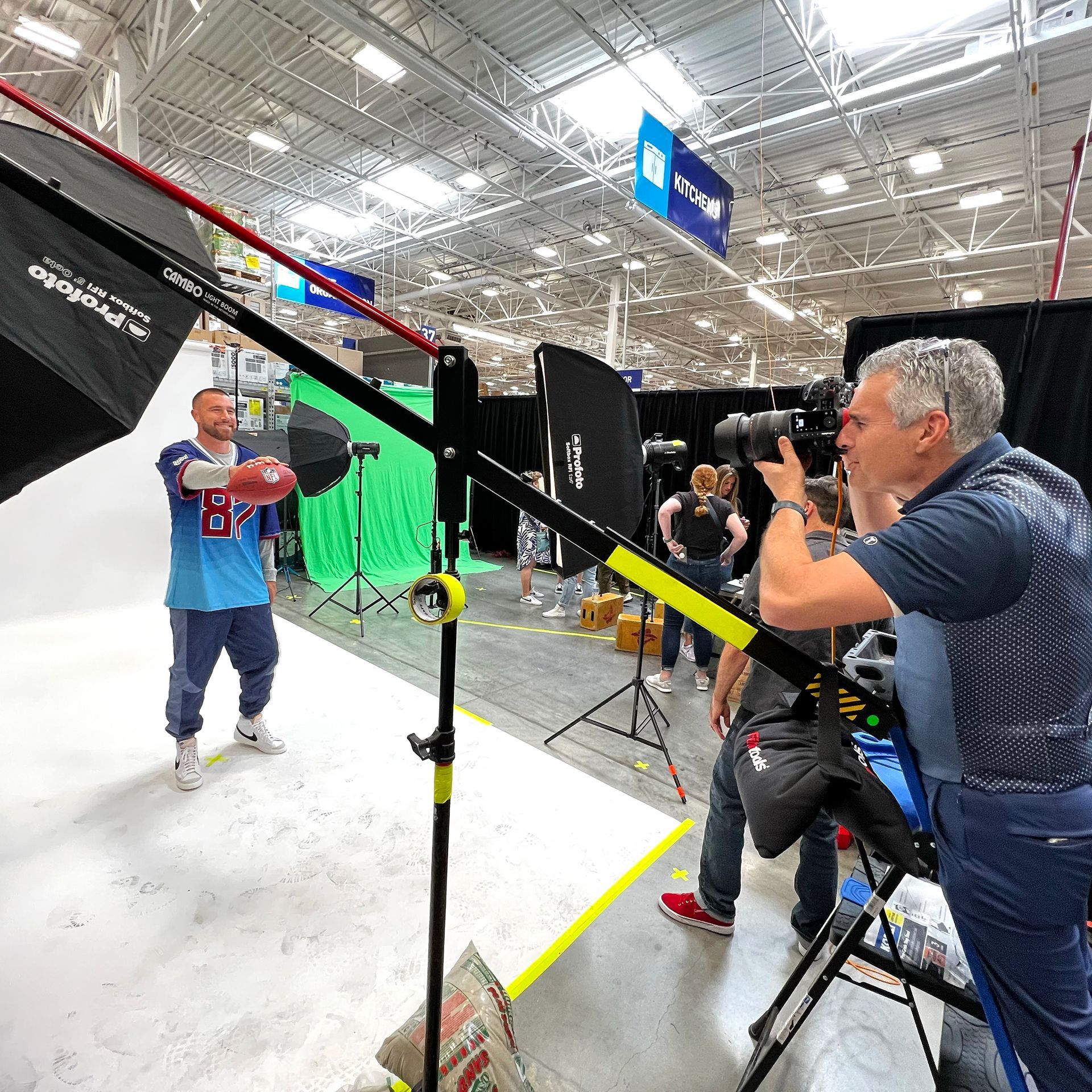 Commercial photographer on location in a retail store is taking photos of a football player holding a football out in front of him.