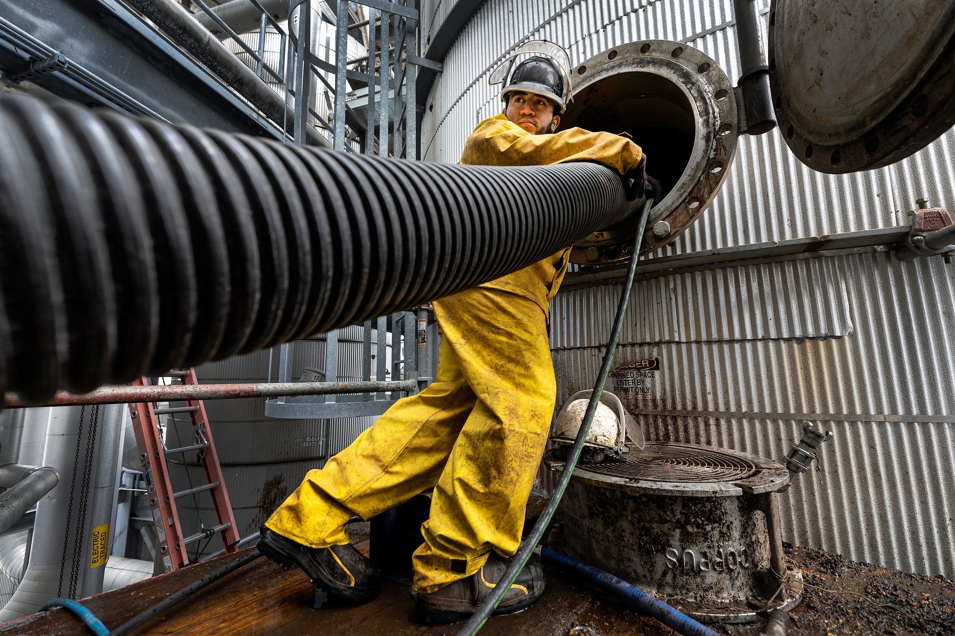 Industrial technician managing high-pressure cleaning equipment during ethanol plant maintenance operations, demonstrating specialized safety protocols and industrial cleaning processes.