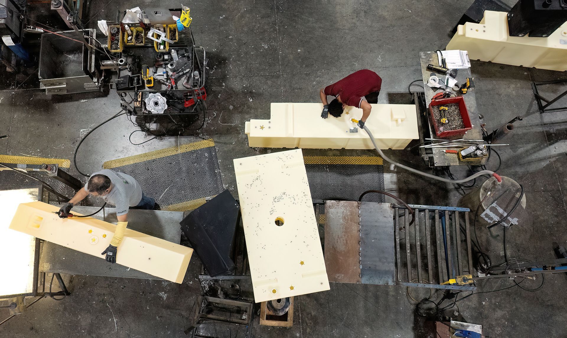 Workers in a manufacturing facility drill holes into large liquid storage containers during the manufacturing process. Photo made using a drone inside of the facility.