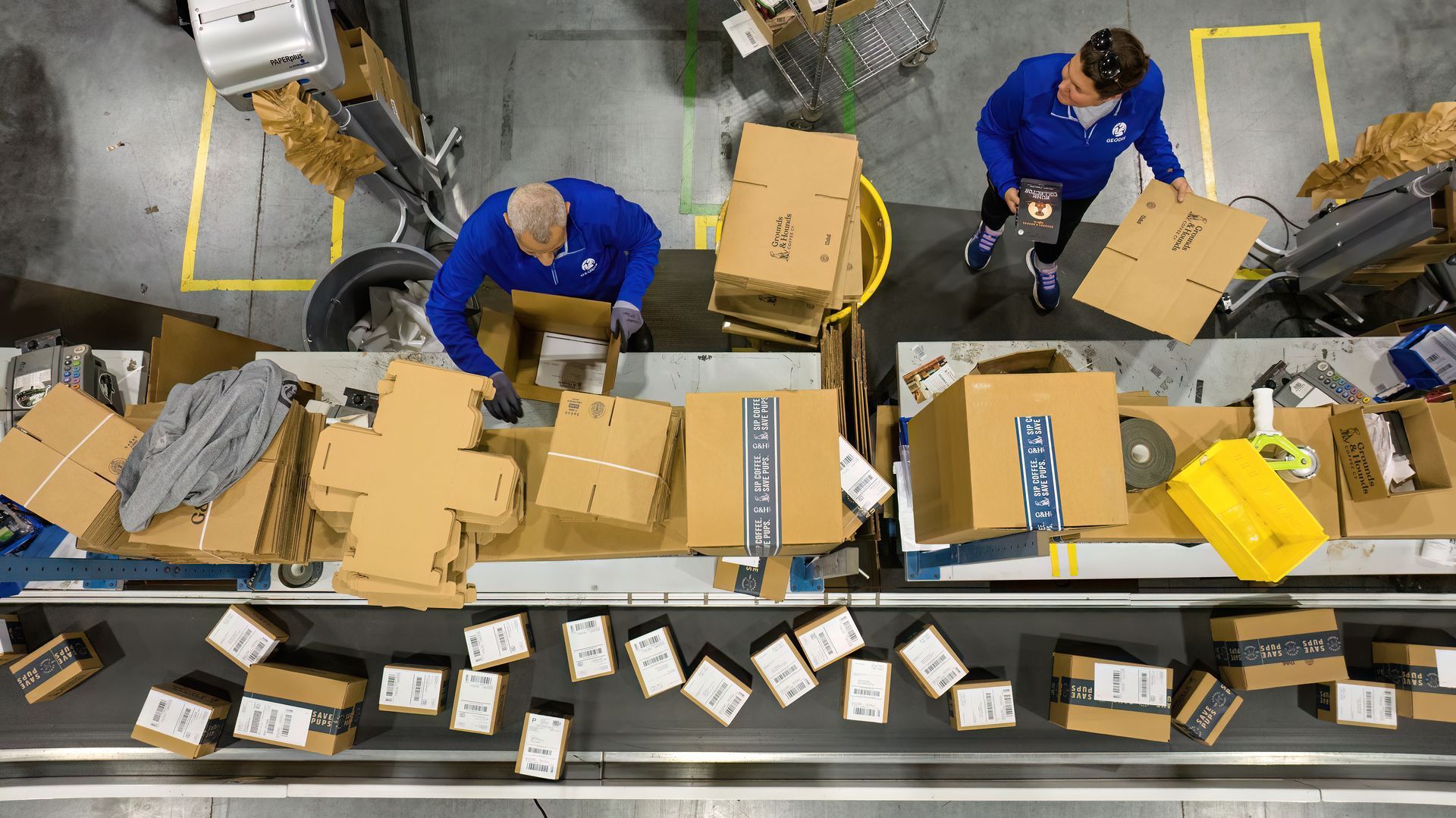 Workers in a product manufacturing facility assemble boxes on an assembly line. Photographer used a drone inside of the facility to create an overhead view of the assembly process. 